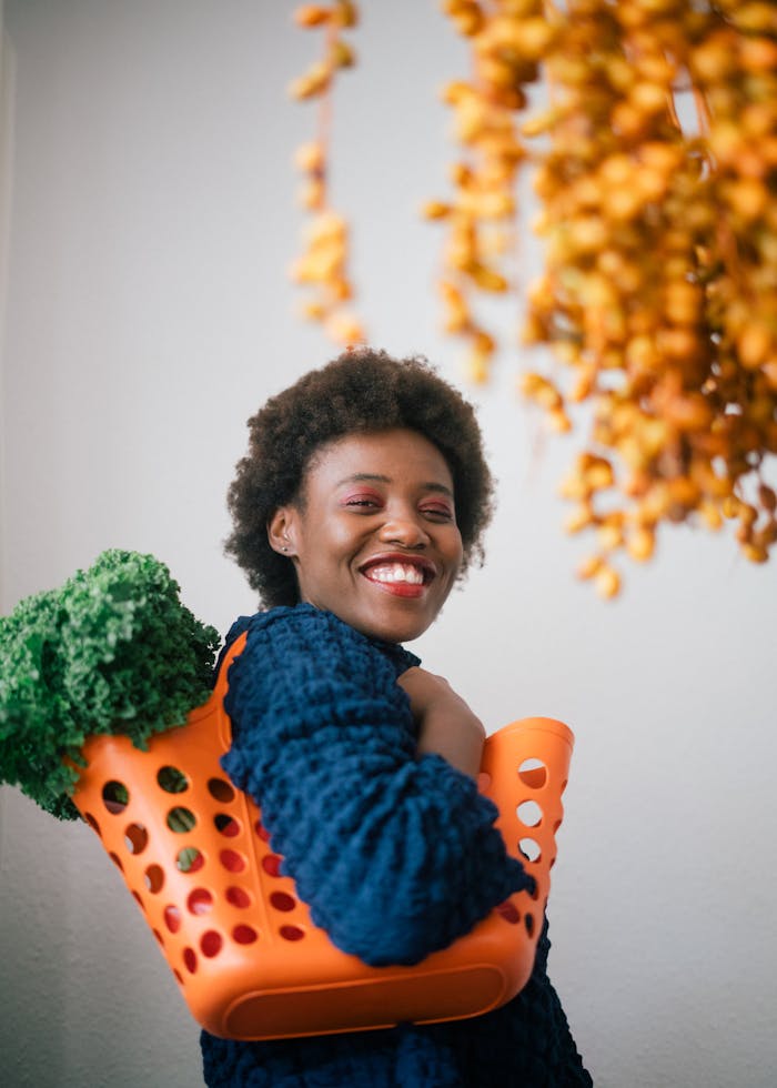 Smiling woman carries fresh green lettuce in an orange basket, enjoying a healthy lifestyle.